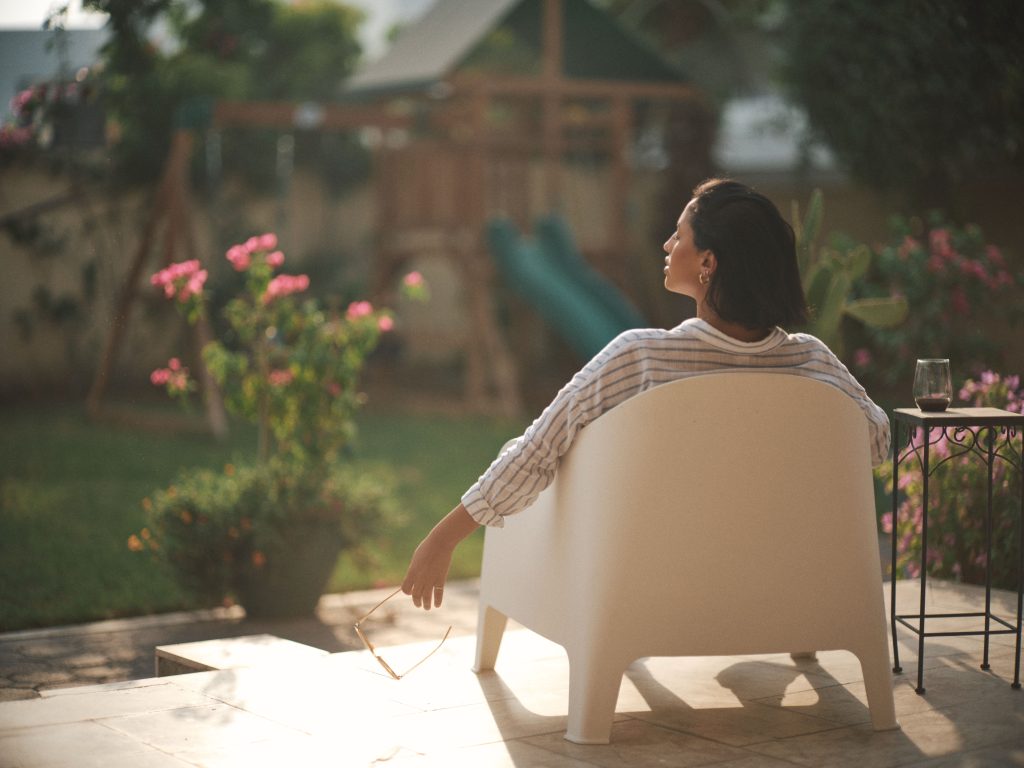 Woman enjoying a quiet moment in a sunlit garden chair, surrounded by nature.